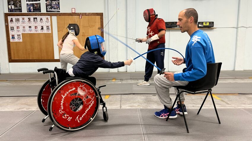 Boy in wheelchair fences with his coach